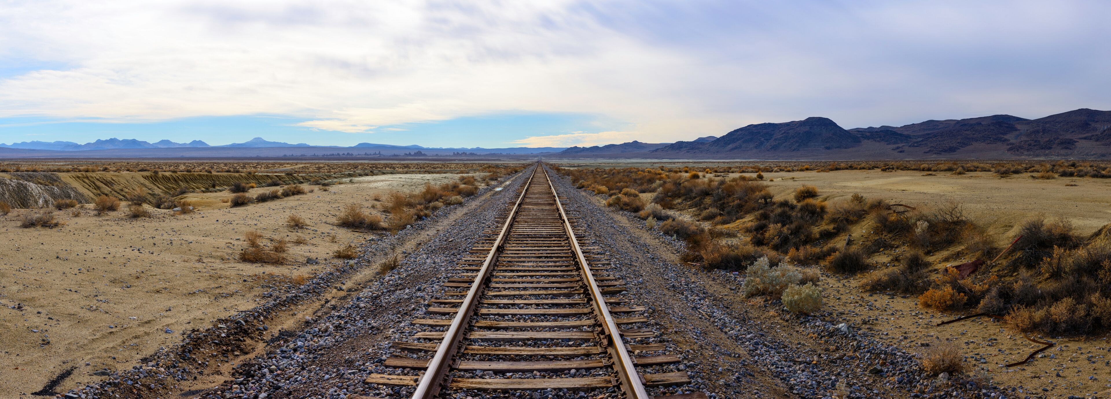 A railway track extending into a desert landscape with mountains in the distance.