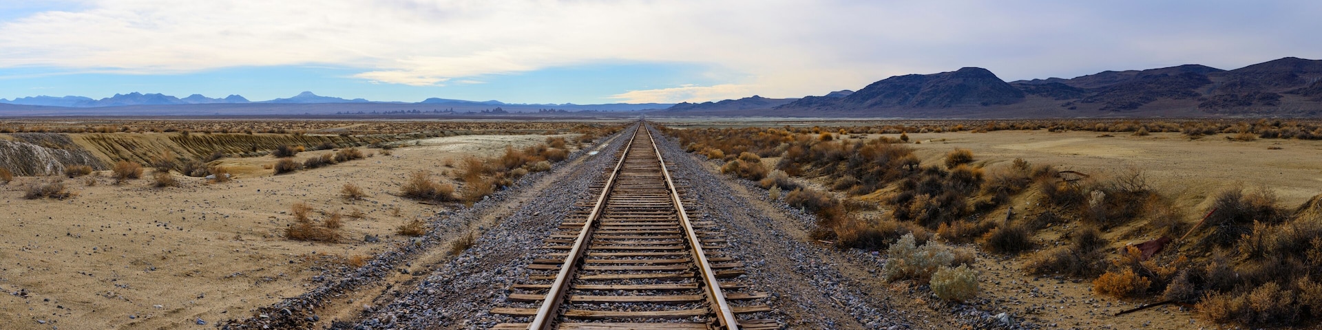 A railway track extending into a desert landscape with mountains in the distance.
