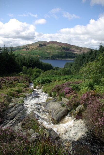 A river flowing through a lush landscape with a lake and hills in the background.