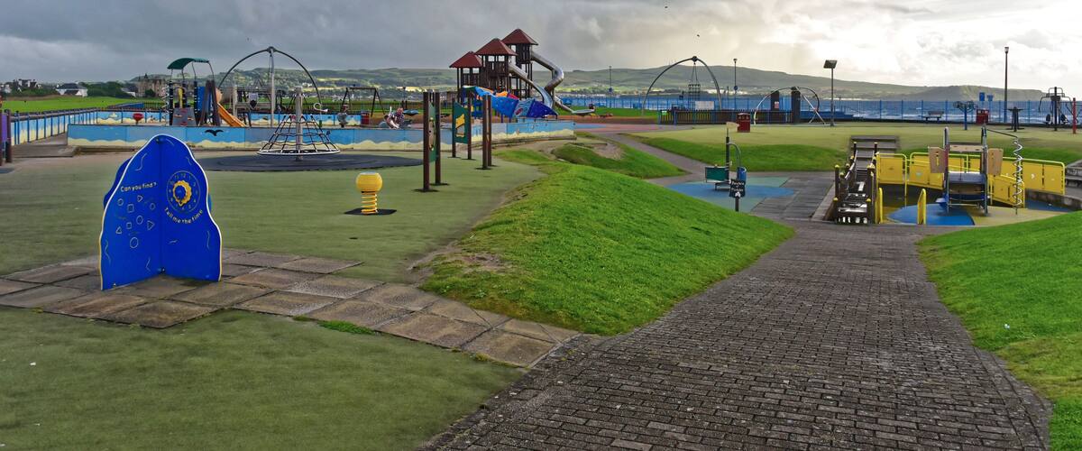 A playground with slides and climbing structures, a blue archway, and a brick pathway.