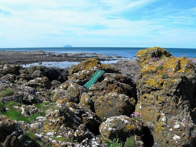 Rocky terrain with a green net, a distant island, and a clear sky.