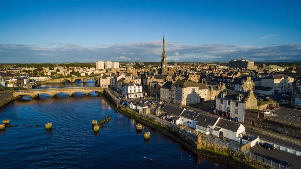 A river with a bridge, a tall church spire, and historic buildings along the riverbank.