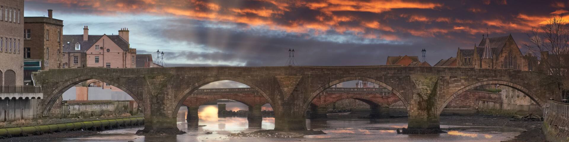 A stone bridge over a river with a sunset sky.