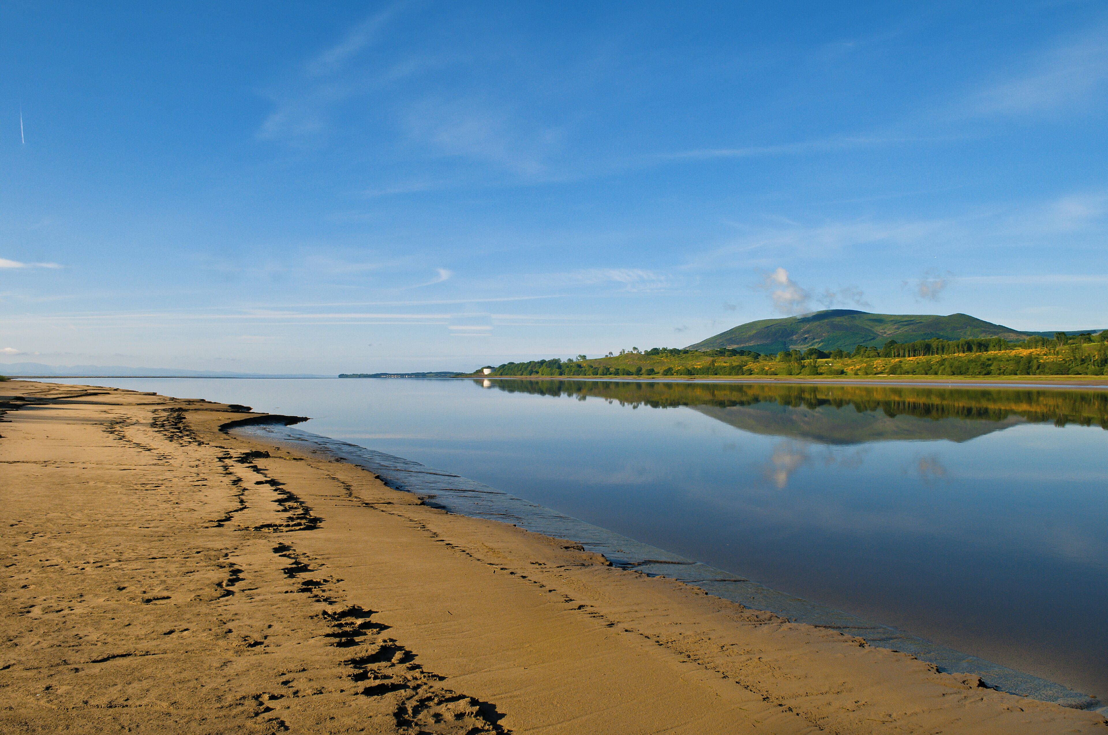 Un lago tranquilo con una playa de arena y una montaña al fondo.