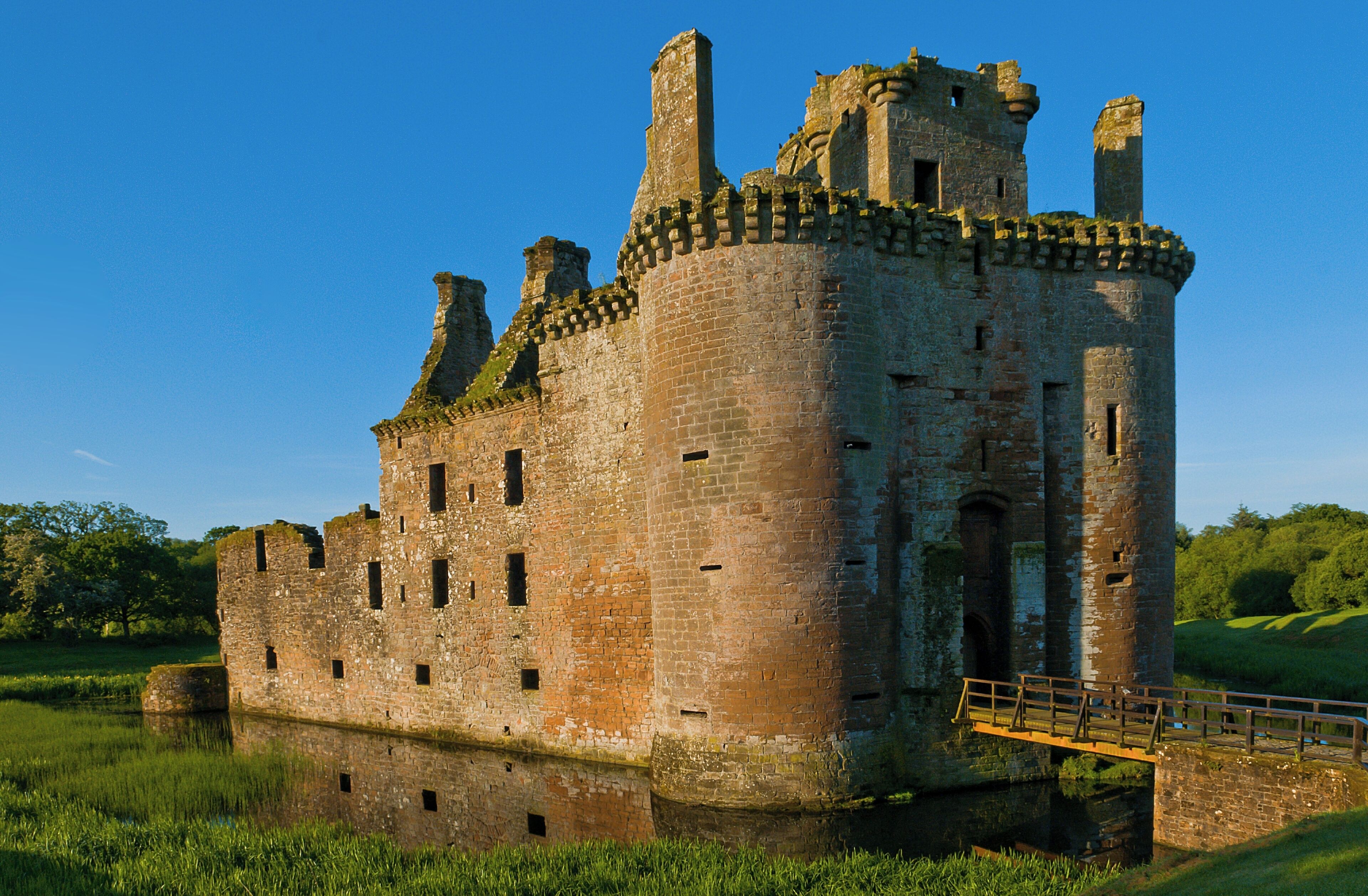 A historic castle with a moat, surrounded by lush greenery.