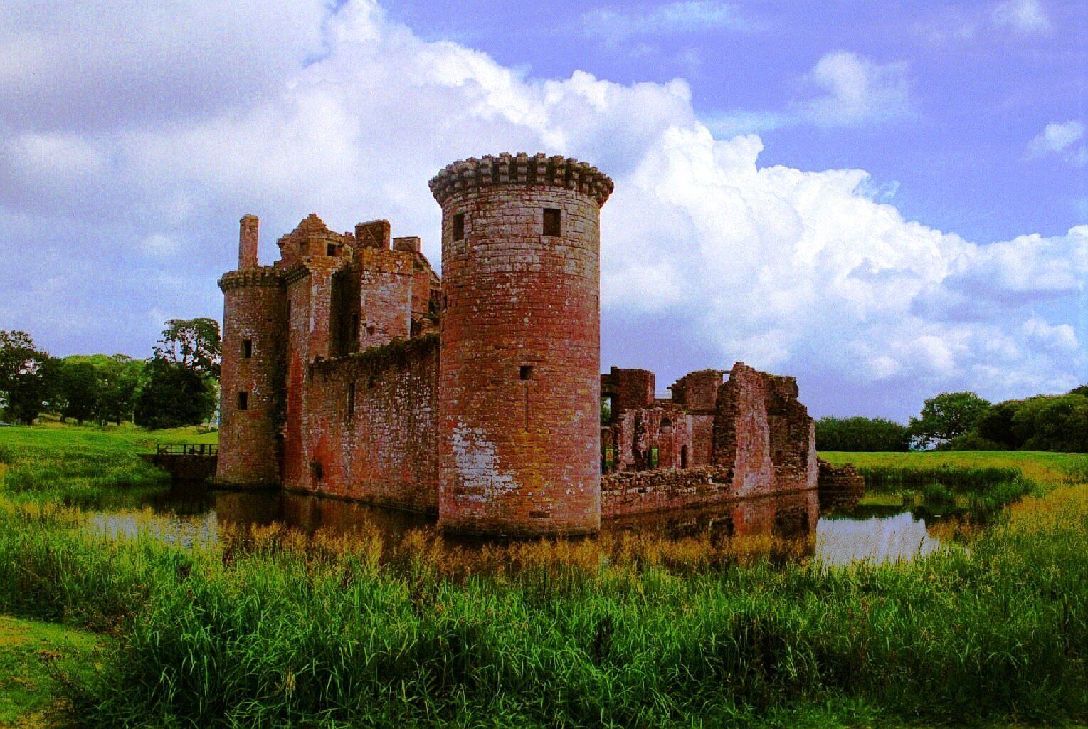 A historic castle ruin surrounded by a moat and lush greenery.