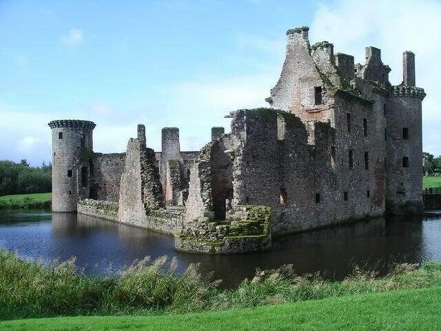 A historic castle with a moat, surrounded by lush greenery.