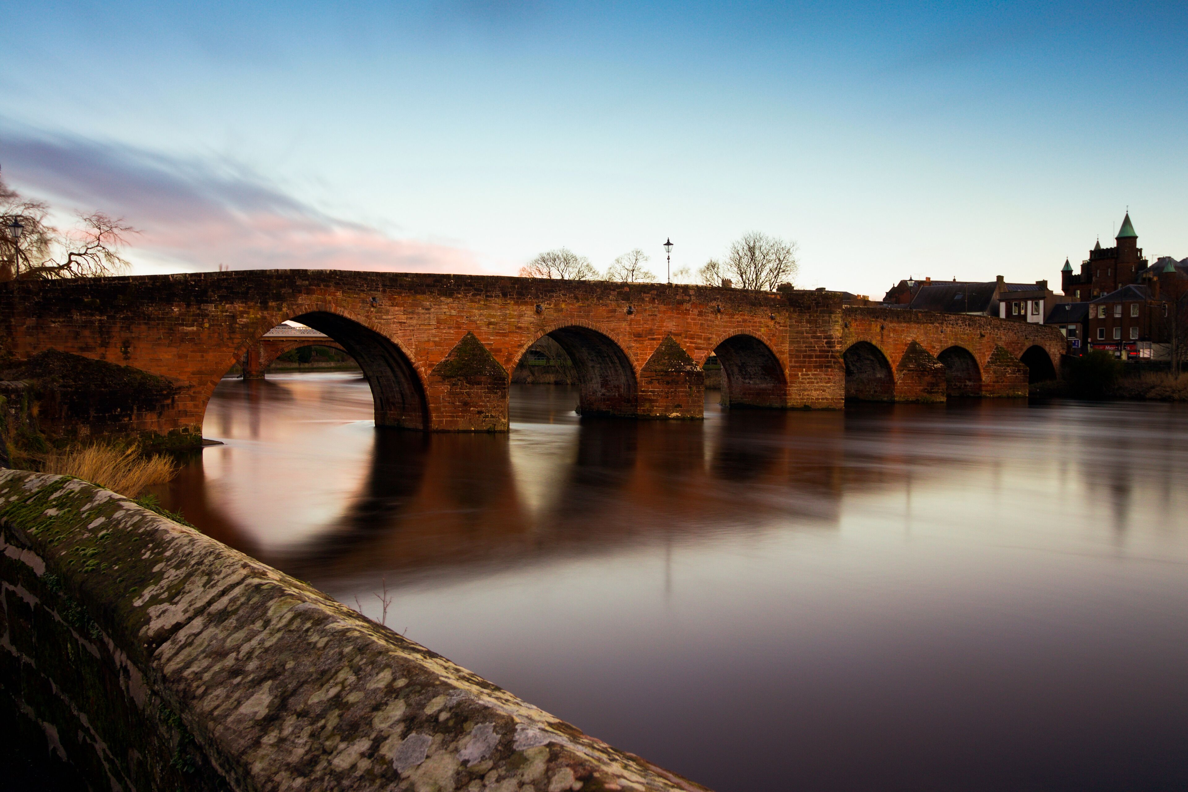 Un pont de pierre enjambe une rivière paisible, avec une ville en arrière-plan.