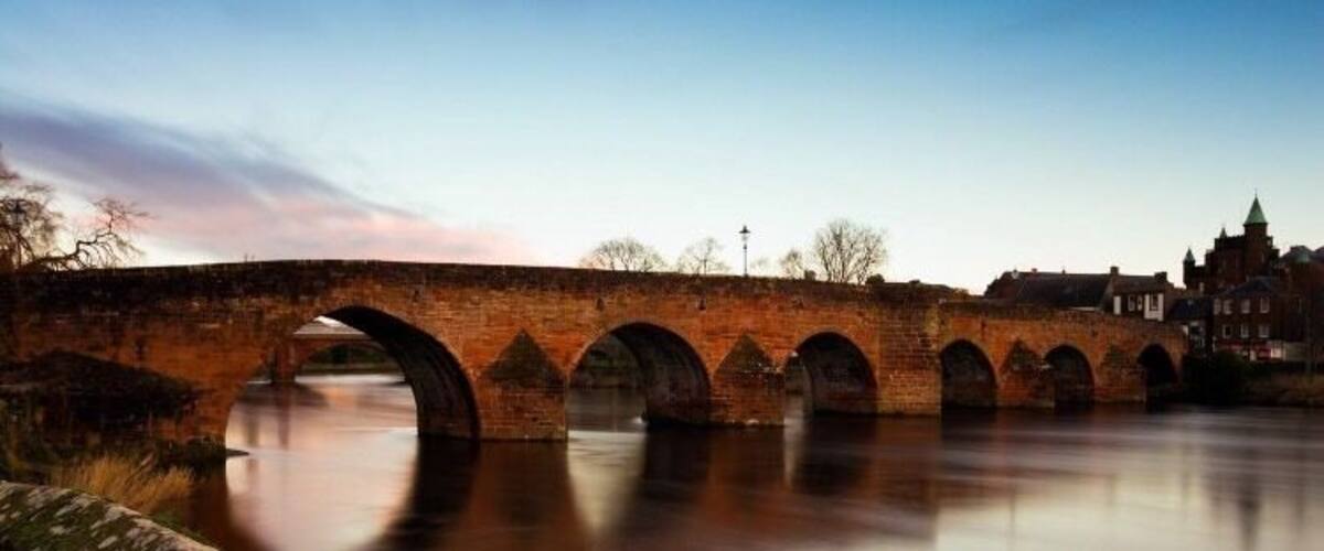 A stone bridge over a calm river with a clear sky.