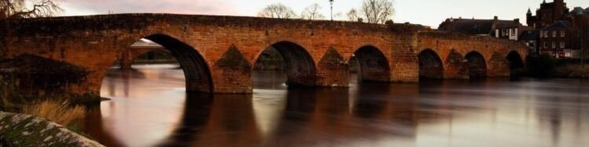 Un puente de piedra sobre un río tranquilo con cielo despejado.