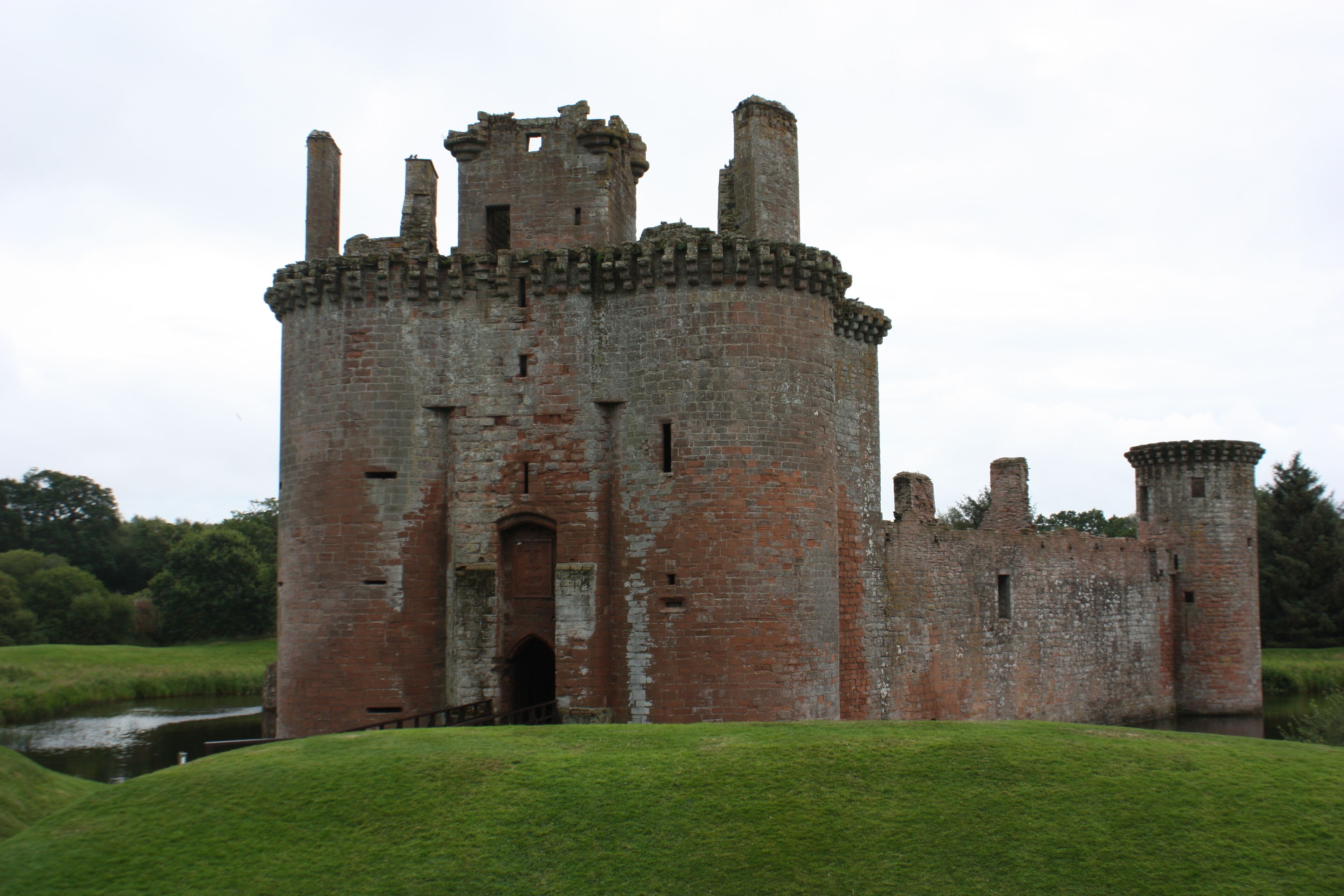 A historic castle with a round tower, surrounded by a grassy area and a small body of water.