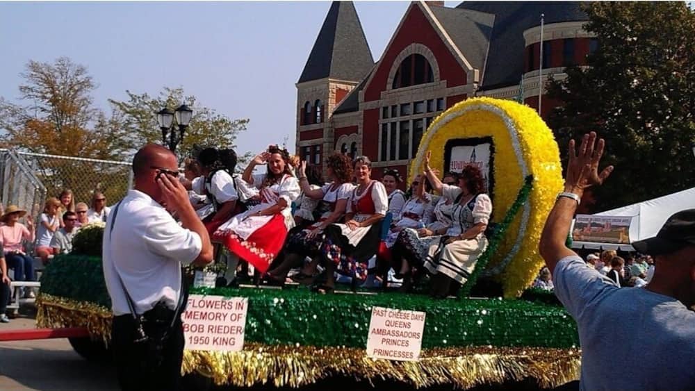 A parade float with a large yellow and green circular decoration and a sign reading "Flowers in Memory of Bob Riedler 1950 King."