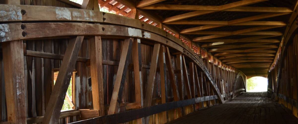 A wooden covered bridge with a curved wooden railing and a wooden floor.
