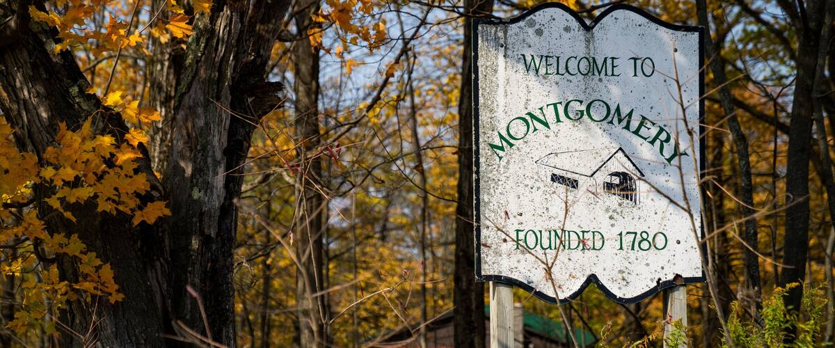 A welcome sign for Montgomery with a house illustration and founding year 1780, surrounded by autumn trees.