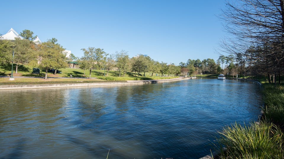 A calm river with grassy banks, trees, and a distant building.