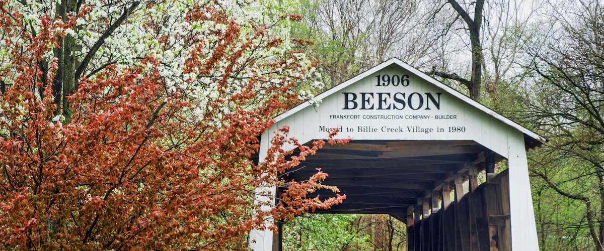 A covered bridge labeled "1906 BEESON" with a sign stating it was moved to Billie Creek Village in 1980.