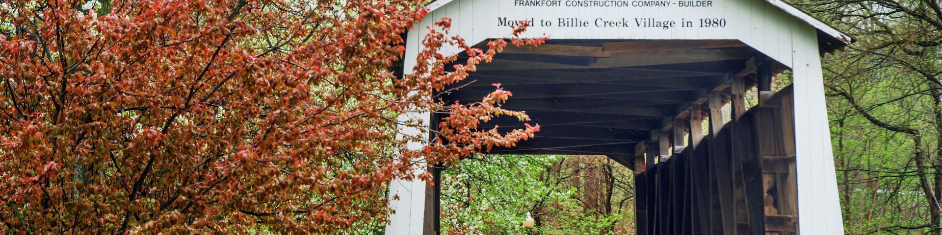 A covered bridge labeled "1906 BEESON" with a sign stating it was moved to Billie Creek Village in 1980.
