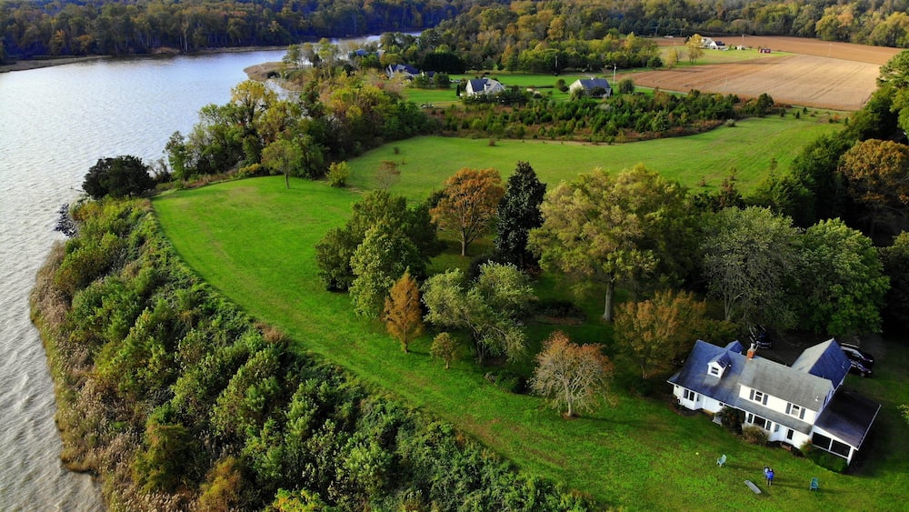 A lakeside property with a large house, green fields, and dense trees.