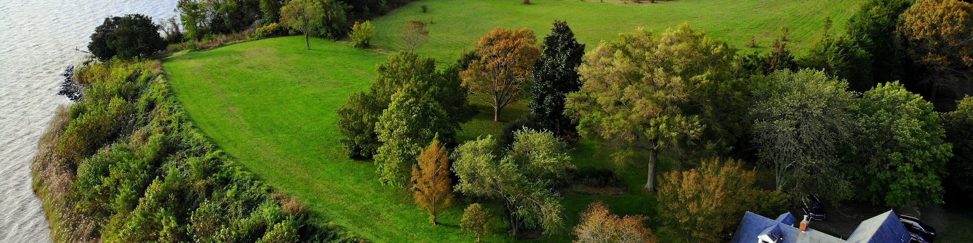 A lakeside property with a large house, green fields, and dense trees.