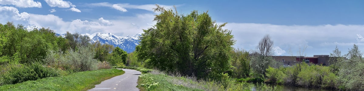 Jordan River Parkway Trail, Redwood Trailhead bordering the Legacy Parkway Trail, panorama views with surrounding trees and silt filled muddy water along the Rocky Mountains, Salt Lake City, Utah.