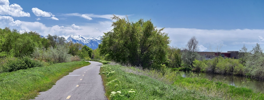 Jordan River Parkway Trail, Redwood Trailhead bordering the Legacy Parkway Trail, panorama views with surrounding trees and silt filled muddy water along the Rocky Mountains, Salt Lake City, Utah.