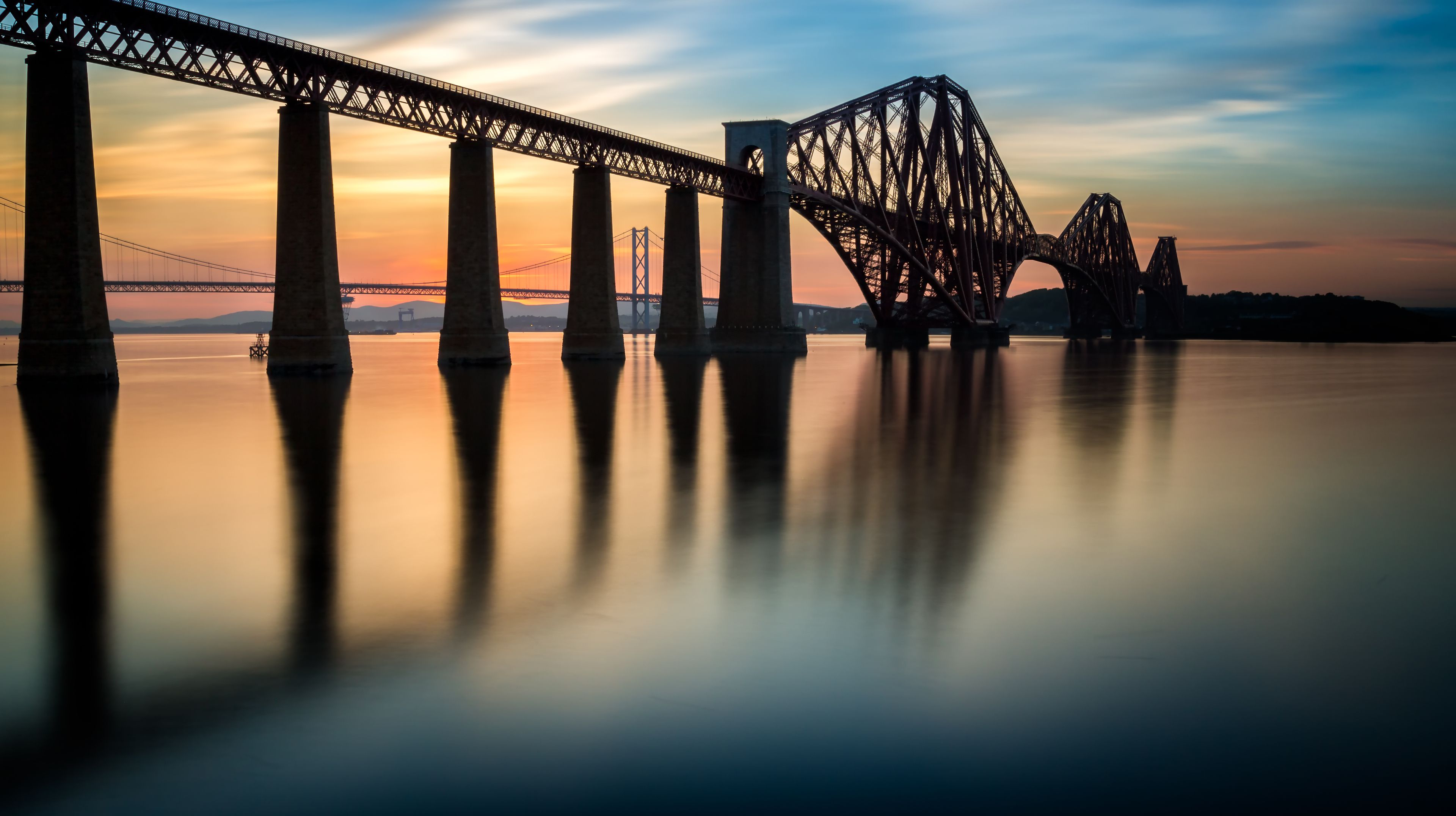 A bridge with multiple arches over a calm body of water during sunset.