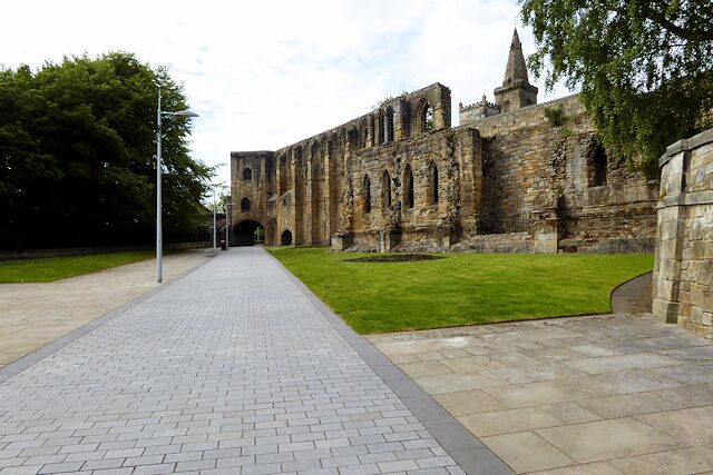 A paved pathway leading to an ancient stone building with a pointed tower.