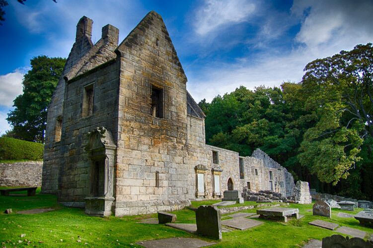 A stone building with a steep roof, surrounded by a cemetery with headstones.