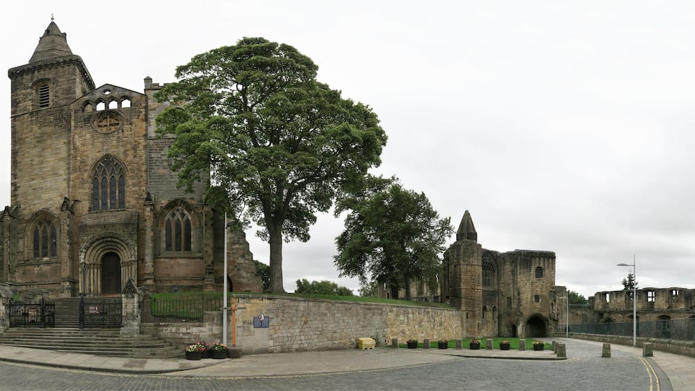 Eine historische Steinkirche mit einem großen Baum davor.