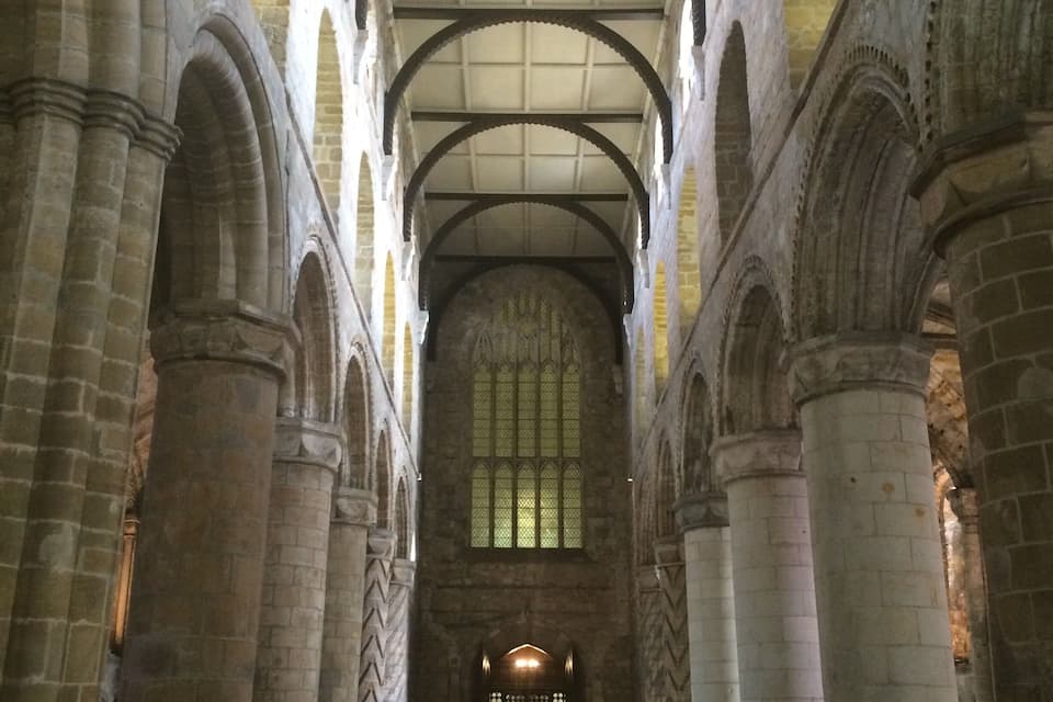 Et indre af et domkirke med hvælvede lofter, stensøjler og et stort farvet glasvindue i midten.