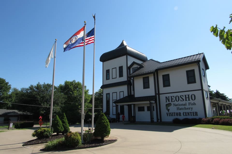 The Neosho National Fish Hatchery Visitor Center with a clear blue sky and flags.
