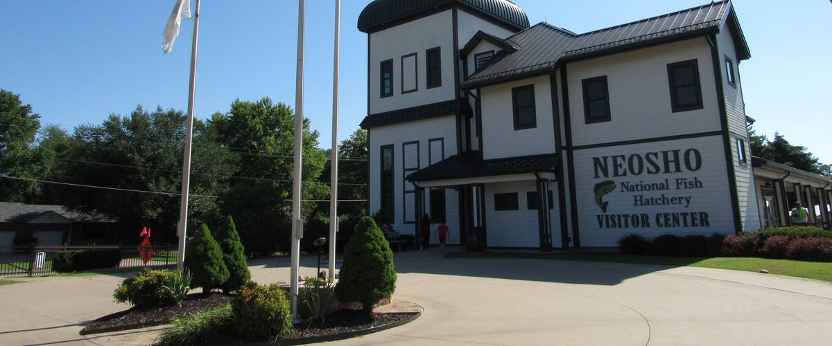 The Neosho National Fish Hatchery Visitor Center with a clear blue sky and flags.