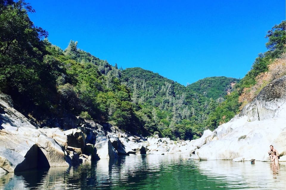A clear river surrounded by rocky terrain and lush greenery.