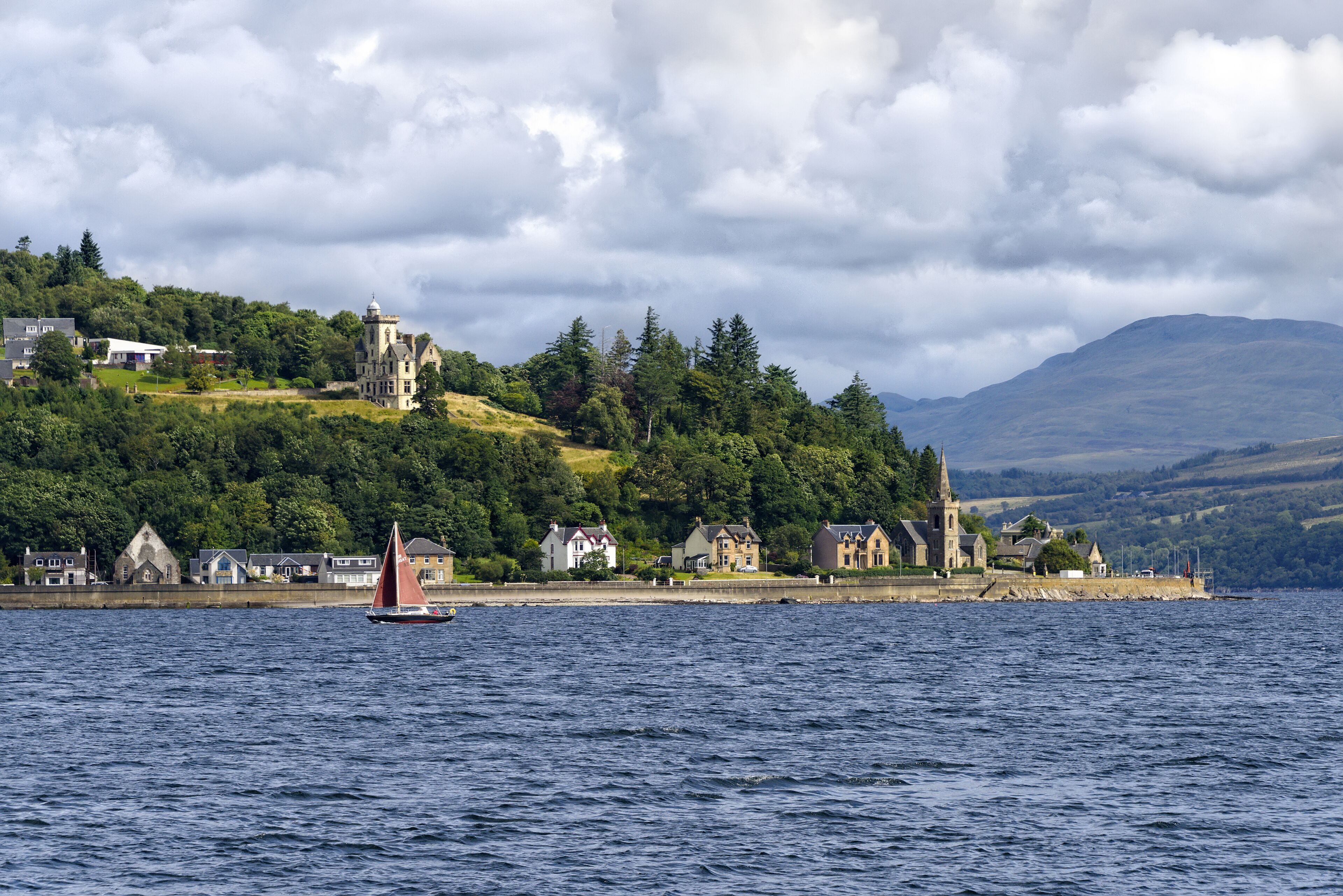 A sailboat on a lake with a historic building and houses on a hillside.