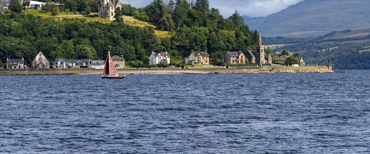 A sailboat on a lake with a historic building and houses on a hillside.