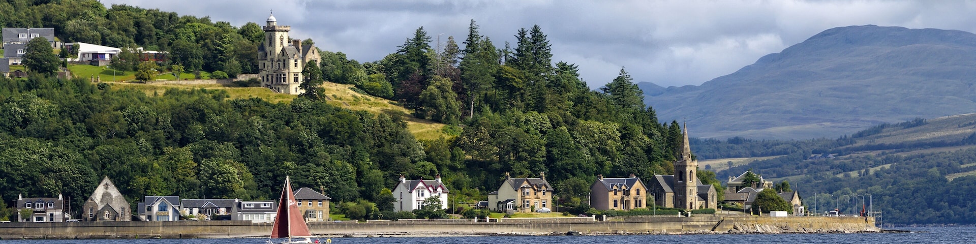 A sailboat on a lake with a historic building and houses on a hillside.