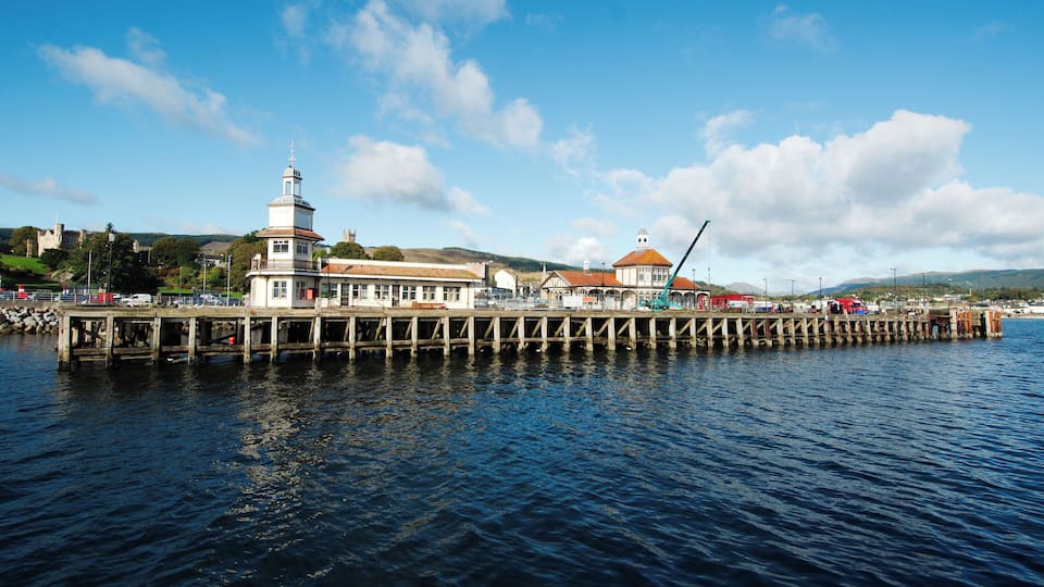 A pier extending into a body of water with a lighthouse and buildings on the right side.