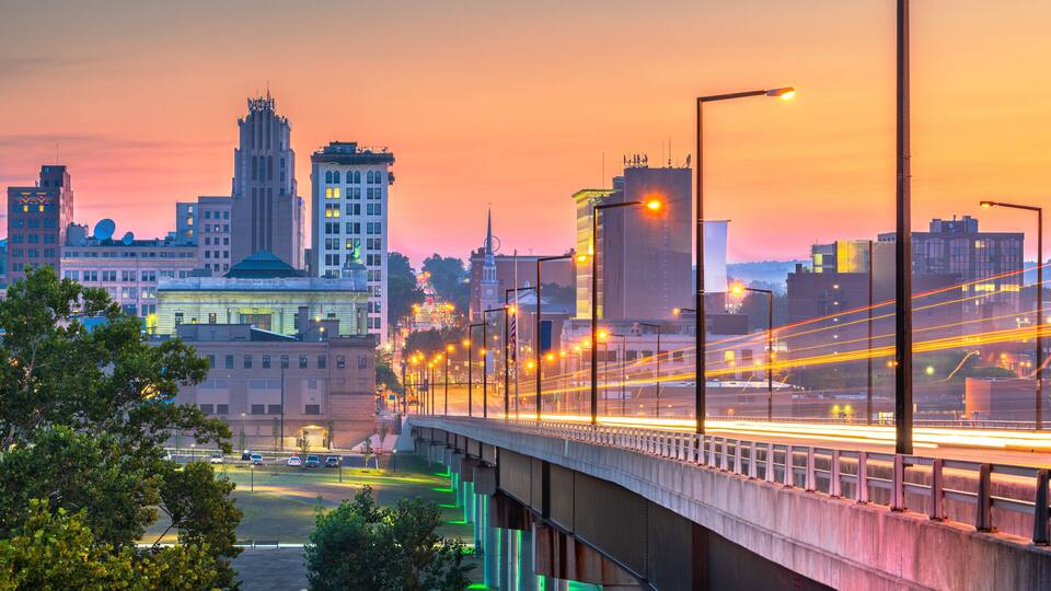A cityscape at dusk with a bridge, buildings, and a river.