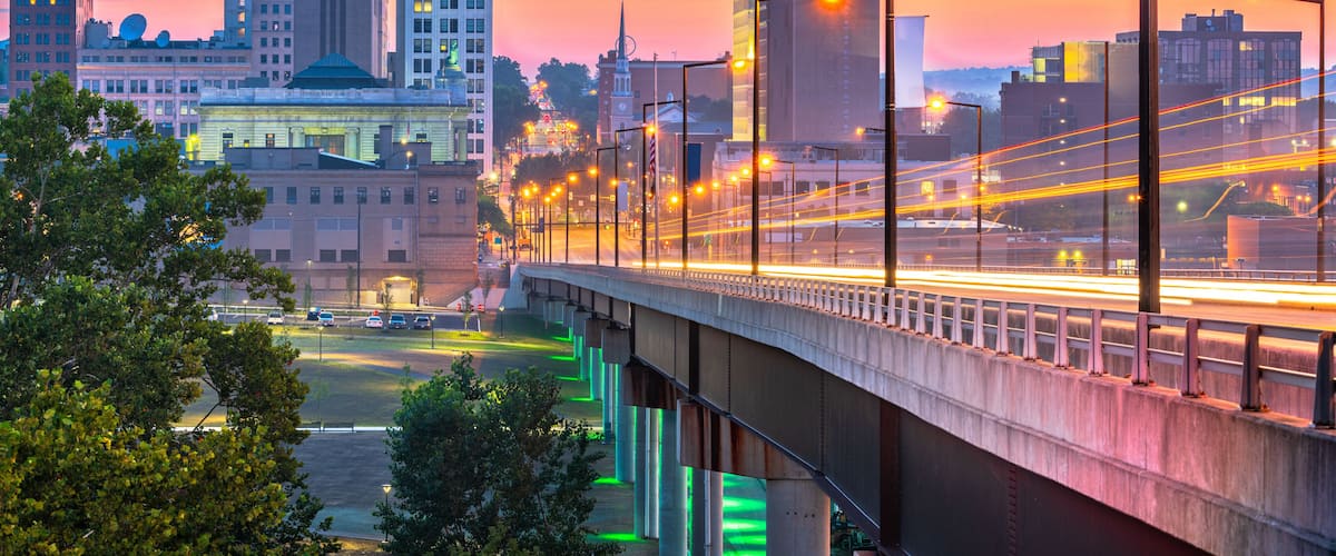 A cityscape at dusk with a bridge, buildings, and a river.