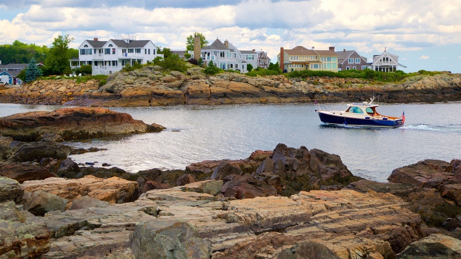 A rocky shoreline with a boat, houses, and a cloudy sky.
