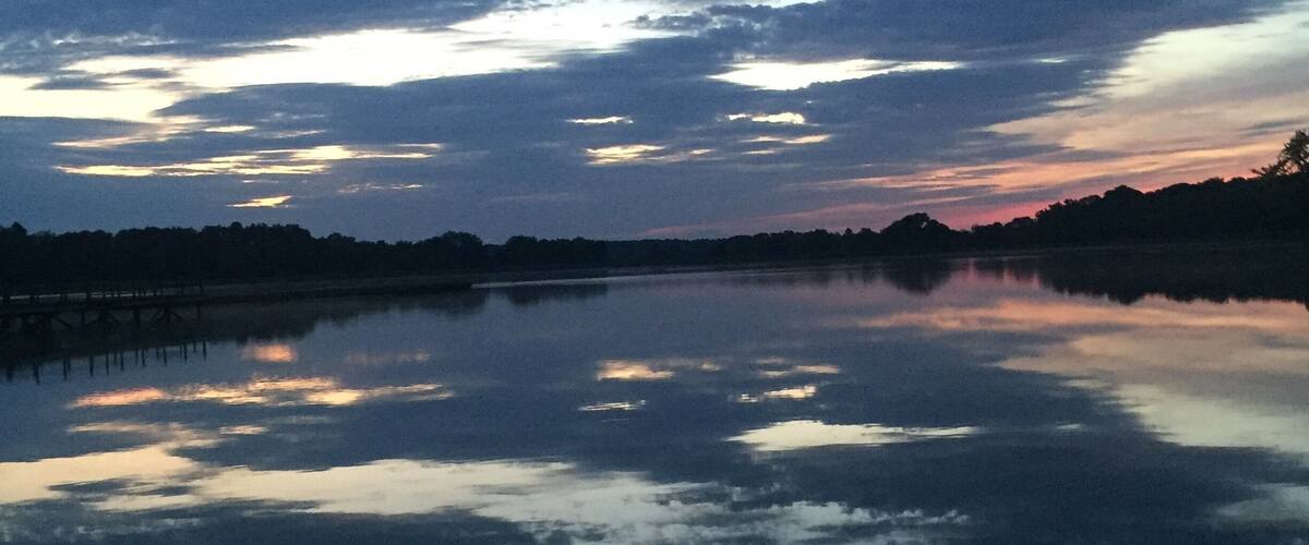A sunset over a calm lake with a pier in the distance.