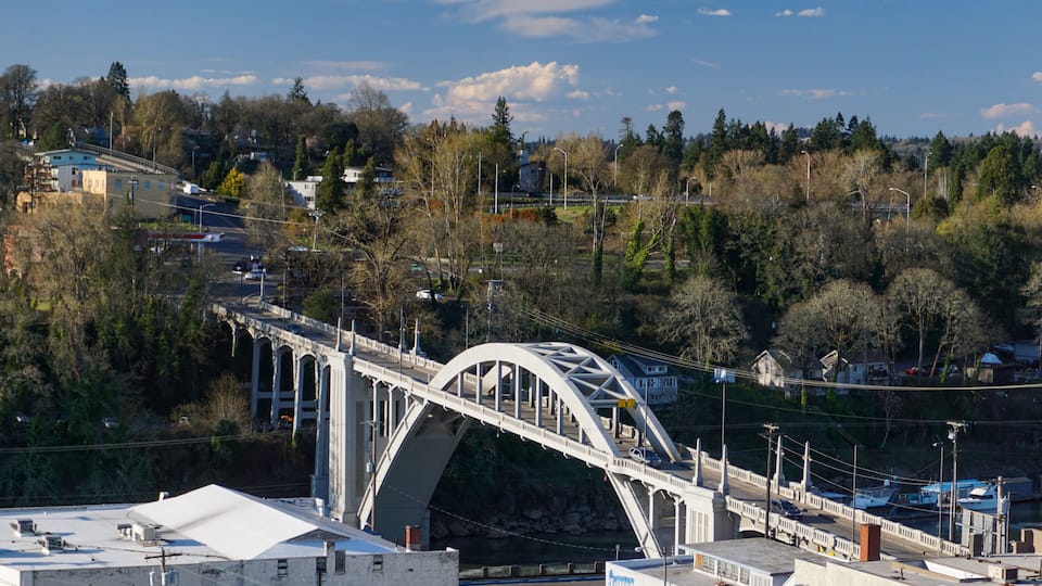 A white bridge with multiple arches spanning a river, surrounded by trees and buildings.