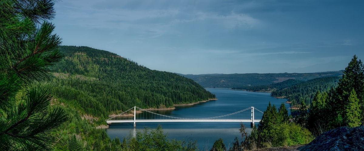 A suspension bridge over a calm lake surrounded by dense forests and hills.