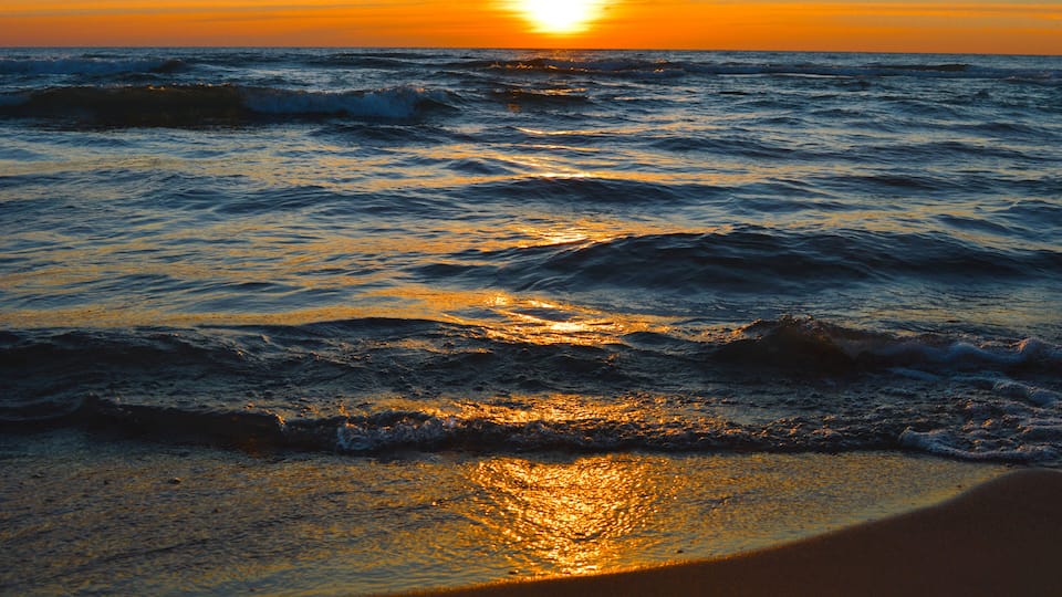 A sunset over the ocean with waves crashing onto the shore.