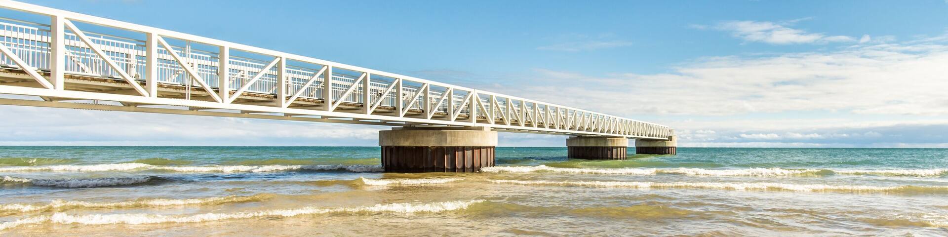 A white bridge over calm ocean waters with a sandy beach.