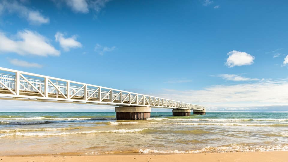 A white bridge over calm ocean waters with a sandy beach.