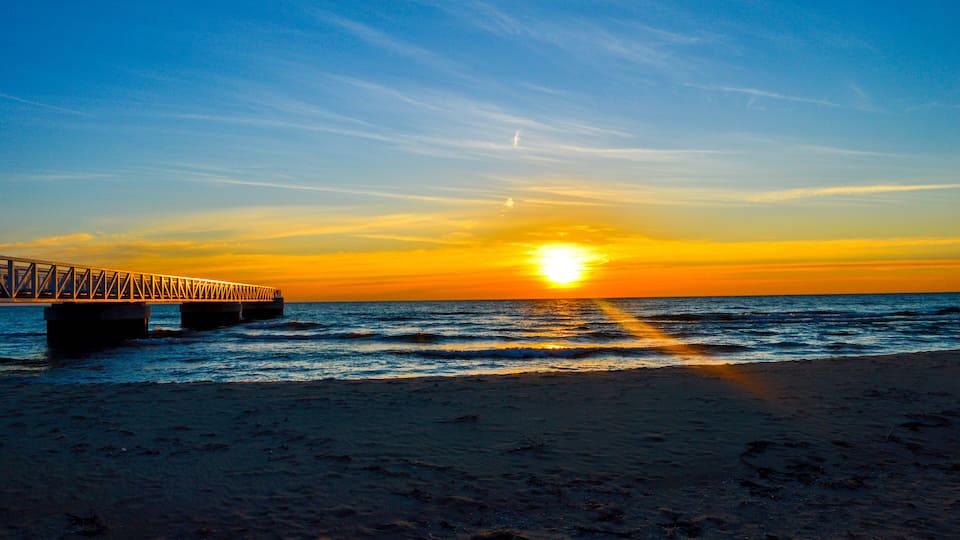 A sunset over the ocean with a bridge in the foreground.