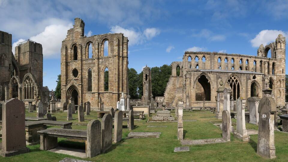 A historic church ruin with Gothic architecture, surrounded by a cemetery with headstones.