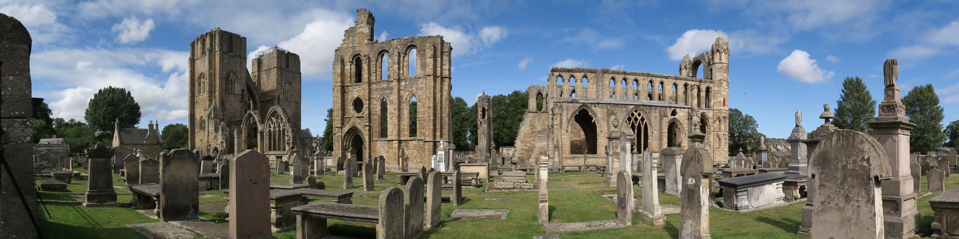A historic church ruin with Gothic architecture, surrounded by a cemetery with headstones.