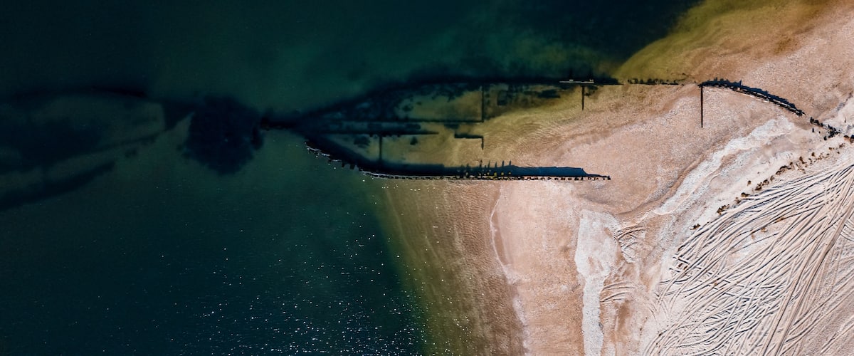 An aerial view of a coastal area with a clear demarcation between land and water, a sandy beach, and a distinct shoreline.
